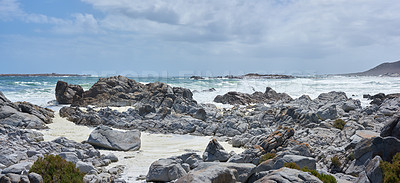 Buy stock photo A rocky coastline at a beach in Cape Town with overcast clouds. A shore with rocks at the ocean with some waves. Rocky coast of mountain sea with on a cold day by a rock pool. 