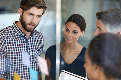 Buy stock photo Shot of coworkers arranging sticky notes on a glass wall during a brainstorming session
