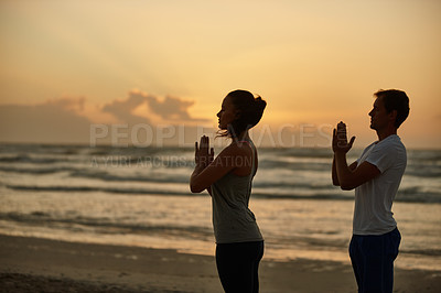 Buy stock photo Shot of a couple doing yoga on the beach at sunset