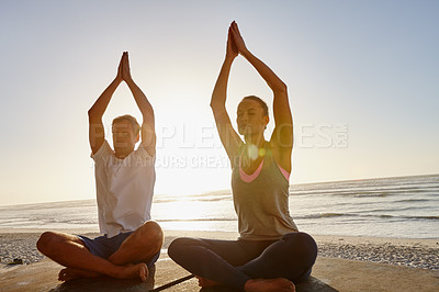 Buy stock photo Shot of a couple doing yoga at the beach at sunset