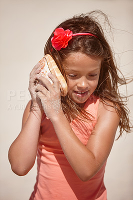 Buy stock photo Shot of a cute little girl holding a seashell to her ear at the beach