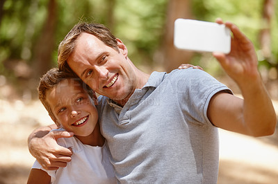 Buy stock photo Shot of a father and son taking a selfie together on a camping trip in the forest