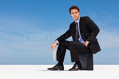 Buy stock photo Thinking, sky and a business man on a briefcase with a newspaper for planning or company vision outdoor. Idea, future and space with a young corporate employee in a suit, sitting on a bag in summer