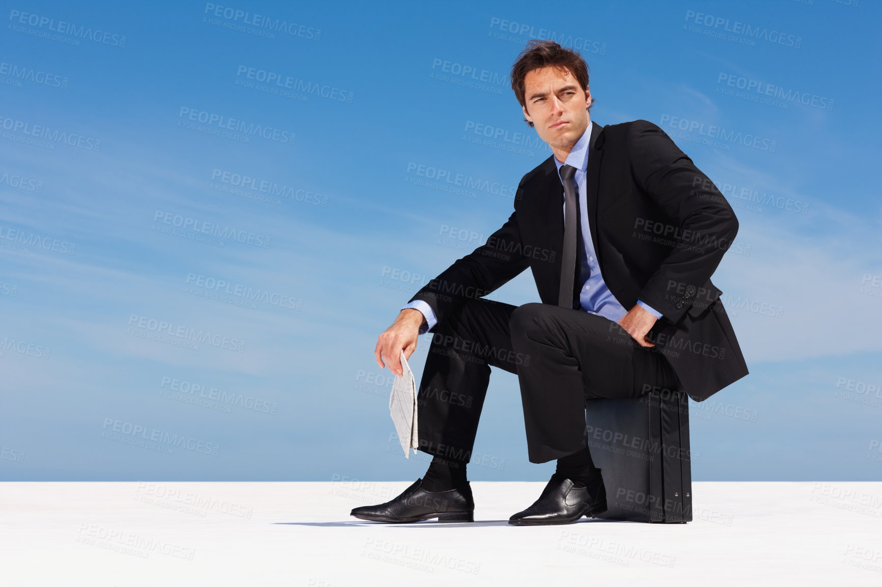 Buy stock photo Thinking, sky and a business man on a briefcase with a newspaper for planning or company vision outdoor. Idea, future and space with a young corporate employee in a suit, sitting on a bag in summer