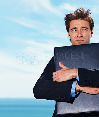 Buy stock photo Travel, stress and business man with briefcase at beach with fear, risk or lost in nature on blue sky background. Appointment, fail and male entrepreneur hugging box at the ocean with anxiety at sea
