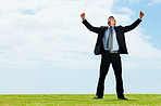 Ambitious business man standing on green grass with his arms outstretched