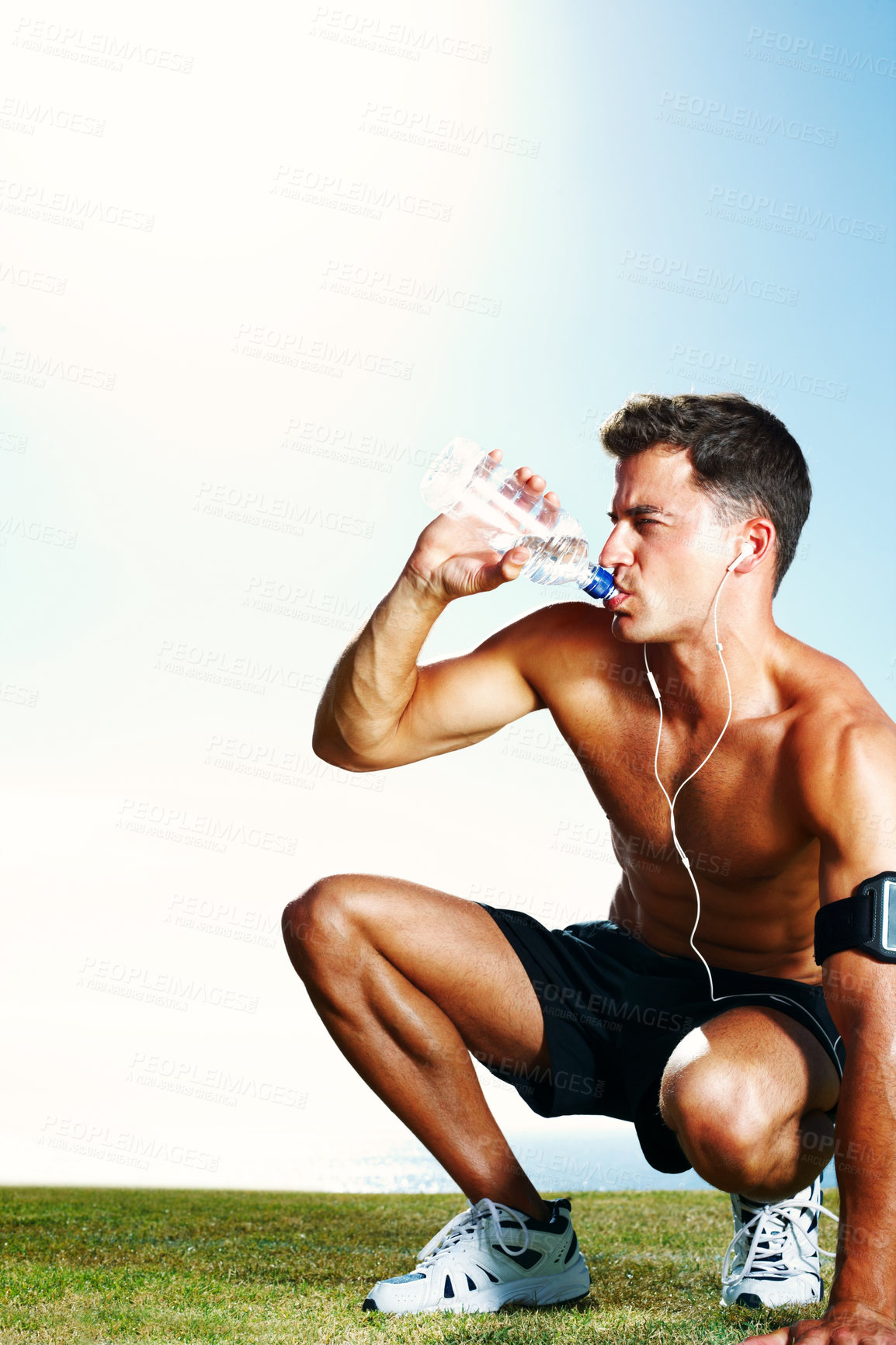 Buy stock photo Water, tired and man on field for workout, earphones and hydration with bottle and summer. Training, cardio and exercise for male person or athlete, running and park for fitness on grass with music