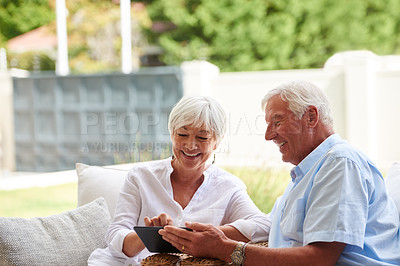 Buy stock photo Shot of a senior couple using a tablet while sitting on their patio