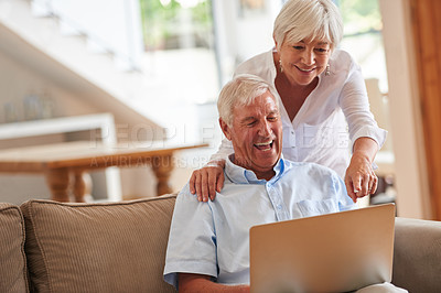 Buy stock photo Shot of a senior woman standing behind her husband who's using a laptop