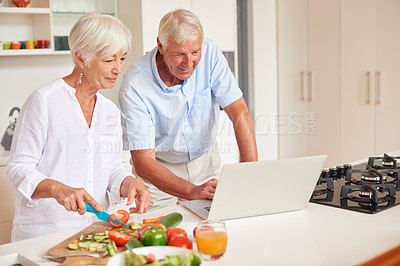 Buy stock photo Shot of a senior couple using a laptop while cooking