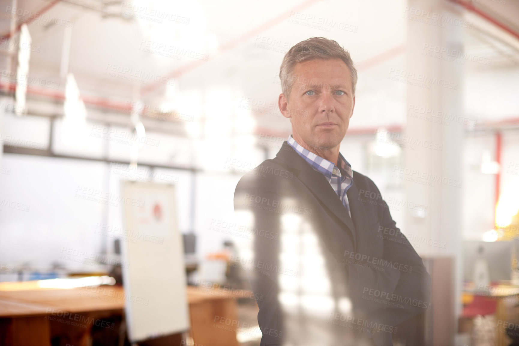 Buy stock photo Cropped through-the-window shot of a businessman standing in an office