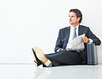 Smart executive sitting against wall with newspaper and briefcase