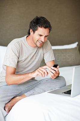 Buy stock photo Phone, social media and laptop with a man in the bedroom of his home to relax on weekend time off. Tech, communication and person sitting on a bed while streaming a movie or series for entertainment
