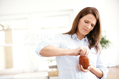 Buy stock photo A mature woman trying to open a jar in the kitchen