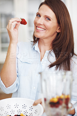 Buy stock photo An attractive woman about to eat a strawberry while preparing a smoothie