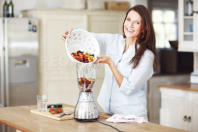 Buy stock photo An attractive woman adding fruit to a blender while standing at a kitchen counter