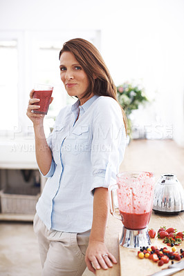 Buy stock photo An attractive woman drinking a fruit smoothie while leaning against a kitchen counter