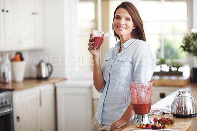 Buy stock photo An attractive brunette enjoying a fruit smoothie while leaning against a kitchen counter