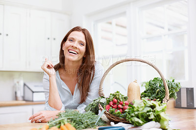 Buy stock photo A beautiful woman smiles at the camera while leaning on the kitchen counter with a basket of vegetables next to her