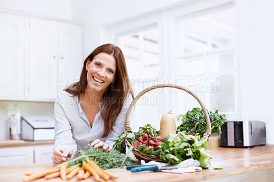 Buy stock photo A beautiful woman leans on her kitchen counter next to a basket of vegetables