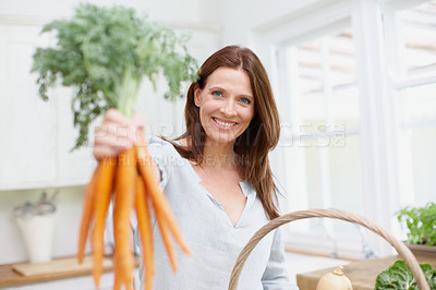 Buy stock photo Portrait of a beautiful woman holding up a bunch of carrots in her kitchen