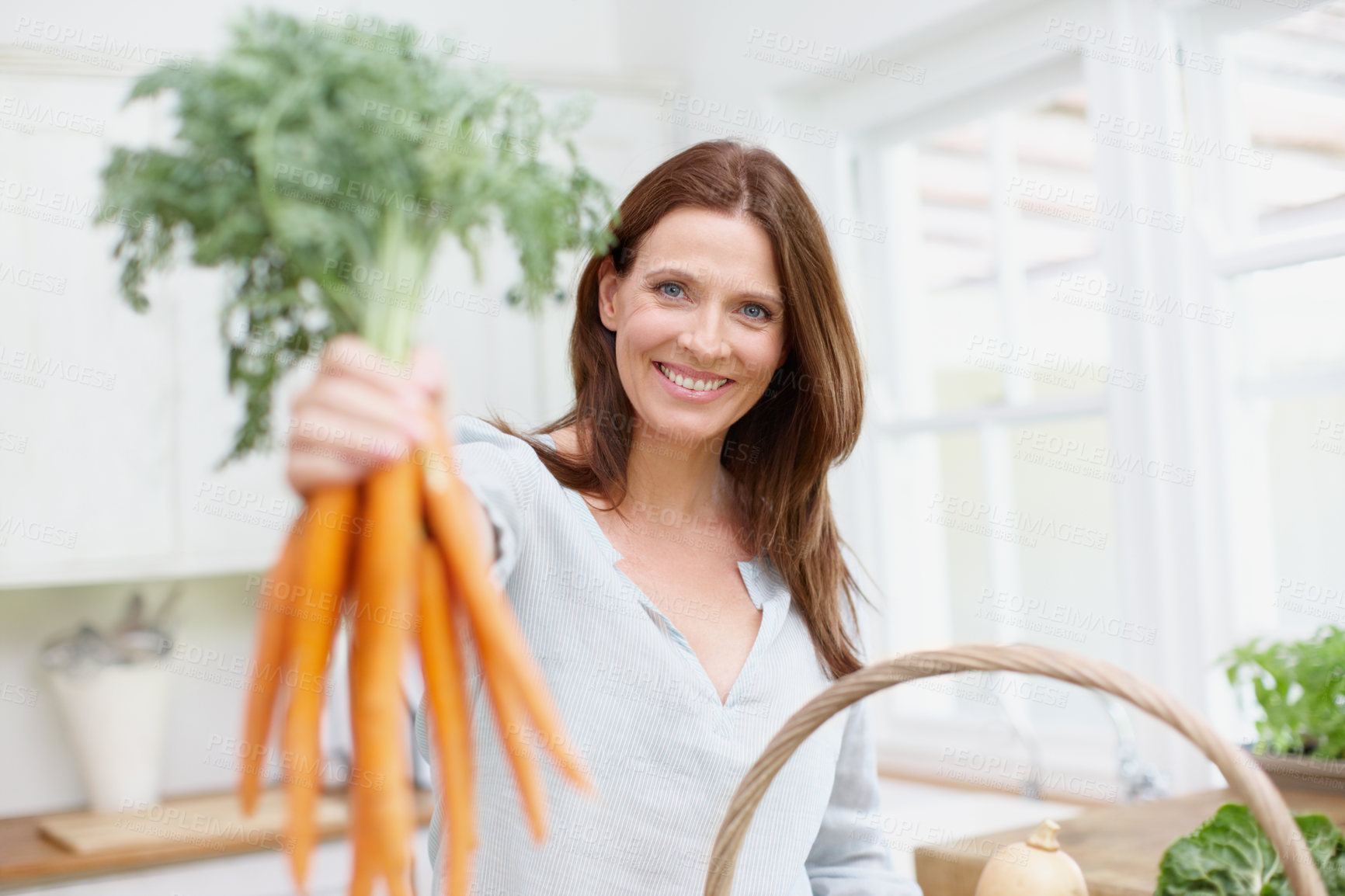 Buy stock photo Portrait, woman and fresh carrots on kitchen table with organic produce, growth and vegetables in basket. Female person, happiness and nutrition for diet, healthy eating and sustainability in home