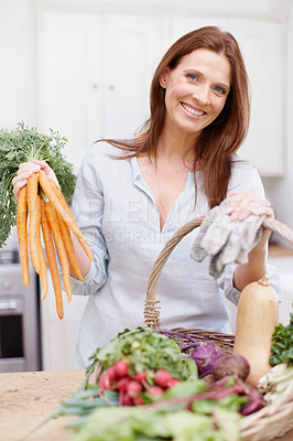 Buy stock photo A beautiful woman proudly standing behind her kitchen counter while holding up the fresh vegetables that she picked