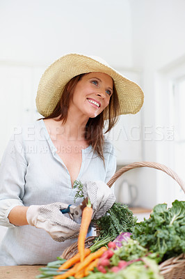 Buy stock photo A gorgeous woman, wearing a straw hat, cuts the stems off fresh vegetables in a basket on the kitchen counter