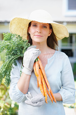 Buy stock photo A beautiful woman in a straw had and gardening gloves holds up a bunch of carrots