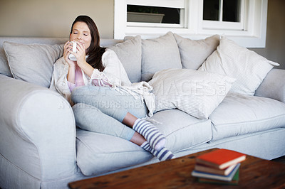 Buy stock photo Portrait of an attractive woman enjoying a cup of coffee while lounging on a sofa indoors