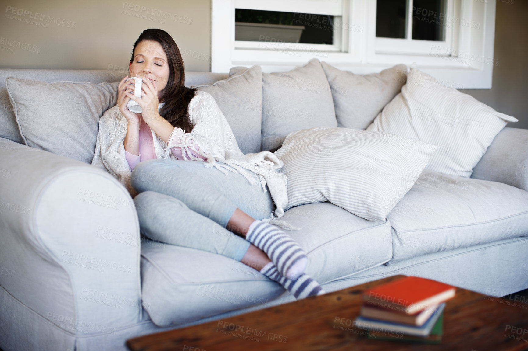 Buy stock photo Portrait of an attractive woman enjoying a cup of coffee while lounging on a sofa indoors