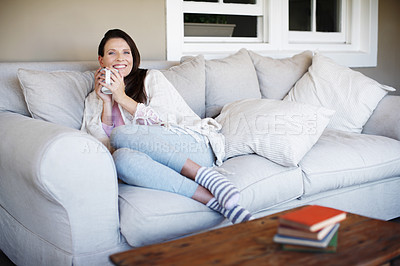 Buy stock photo An attractive woman enjoying a cup of coffee while lounging on a sofa indoors