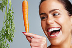Cheerful young woman with carrot against colored background