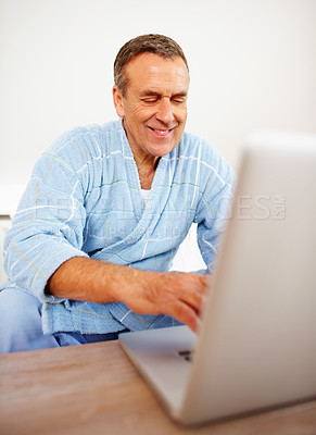 Buy stock photo Home, bathrobe and senior man with a laptop, typing and internet with website information, smile and relax. Apartment, mature guy and person with a pc, morning and happiness with technology and email