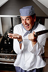 Cheerful senior chef holding knife in front of vent hood