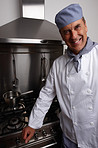 Smiling senior chef standing by gas stove and vent hood