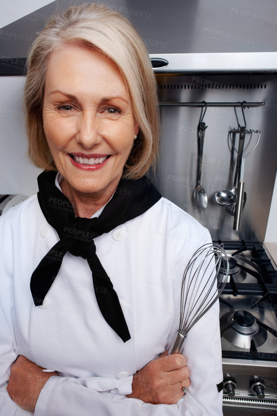 Buy stock photo Closeup portrait of a female chef holding wire whisk standing in front of gas stove