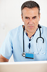 Senior doctor with stethoscope working on laptop against white