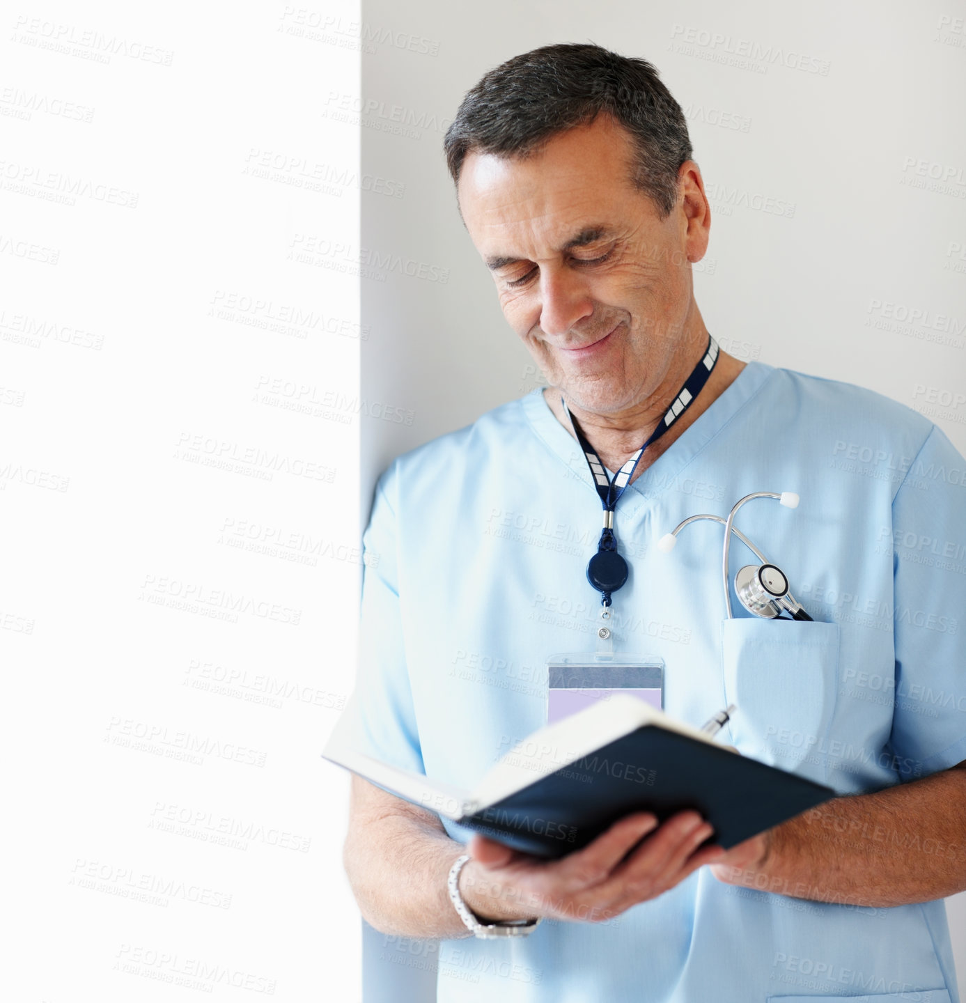 Buy stock photo Portrait of a smiling medical doctor noting schedule while leaning against wall