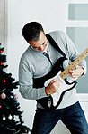 Happy mature man playing guitar with Christmas tree in background