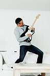 Cheerful mature man standing on sofa playing an acoustic guitar