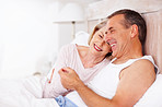 Cheerful mature man holding wife's hand in bed