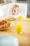 Cute little boy having breakfast with donut and juice on table