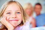 Smiling young girl with hand on chin while parents in background