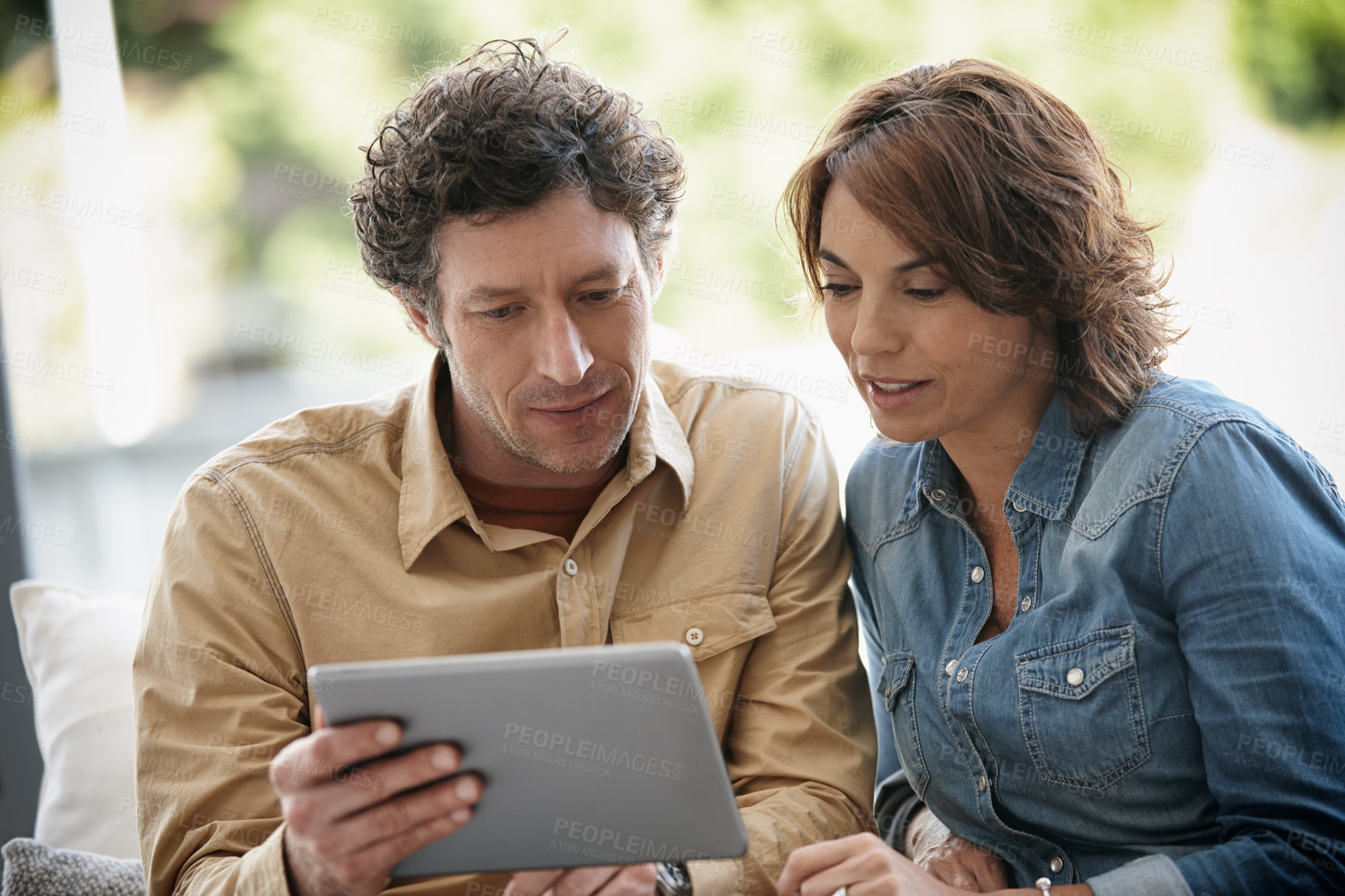 Buy stock photo Shot of a husband and wife using a digital tablet together at home