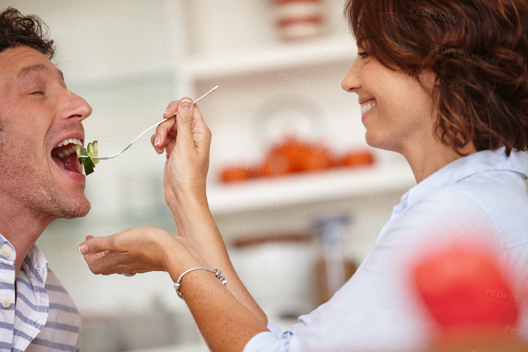 Buy stock photo Shot of a happy wife giving her husband a taste of food