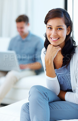 Buy stock photo Portrait of beautiful woman smiling at home with man using laptop in background