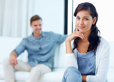 Buy stock photo Beautiful young woman smiling at home with man relaxing in background