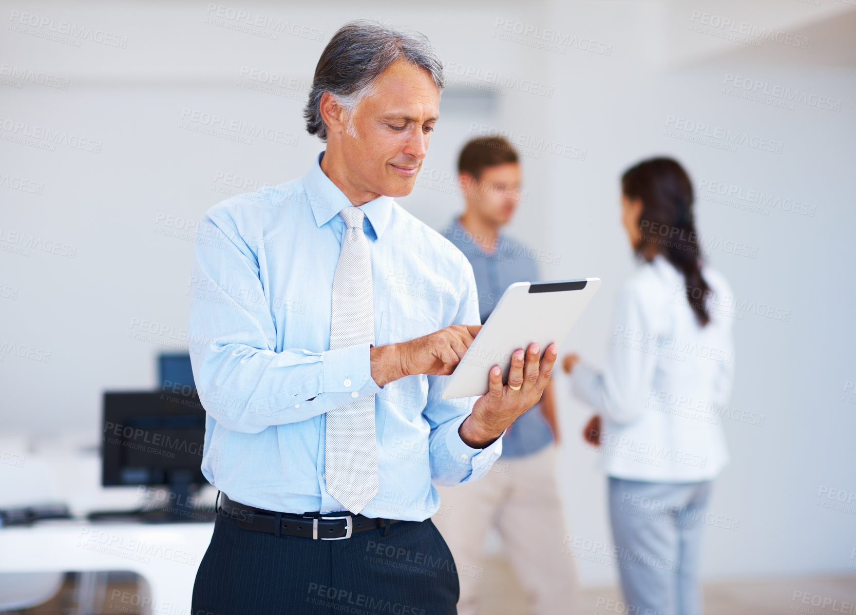 Buy stock photo Portrait of mature business man using electronic tablet with colleagues in background