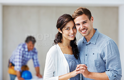 Buy stock photo Portrait of young loving couple smiling holding hands with architect in background
